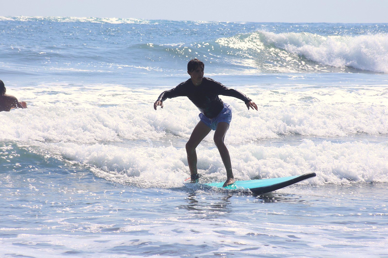 Young surfer standing up on a turquoise board in the whitewater