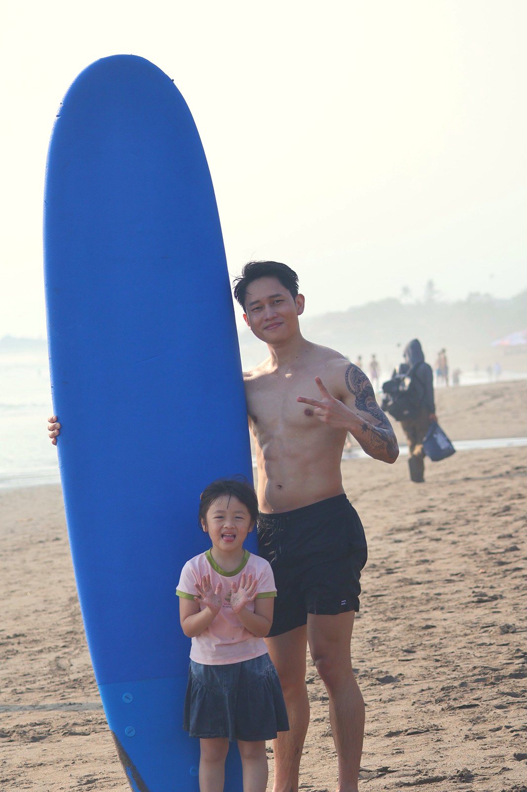 Dad and daughter smiling beside a tall blue surfboard