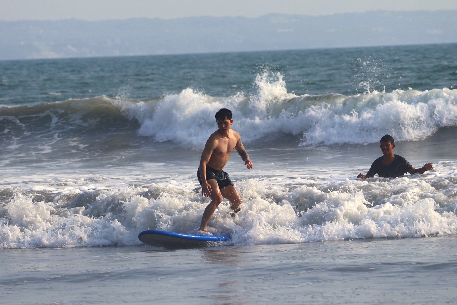 Surfer riding whitewater as his instructor watches from the water