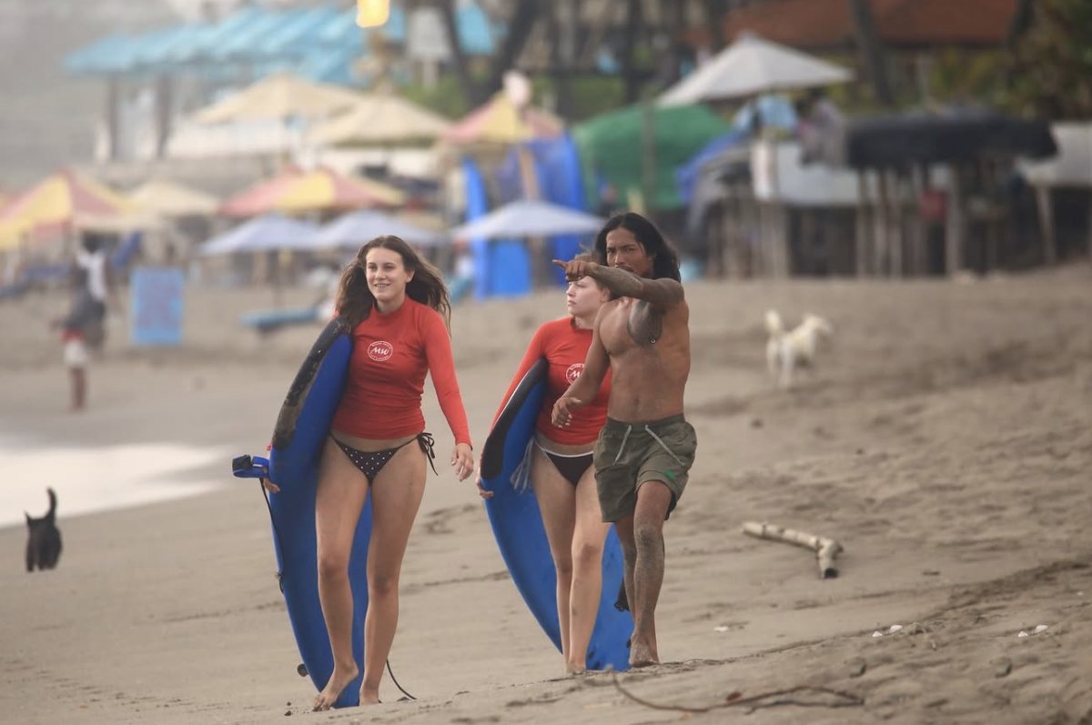 Gov leading two students with their boards along the beach