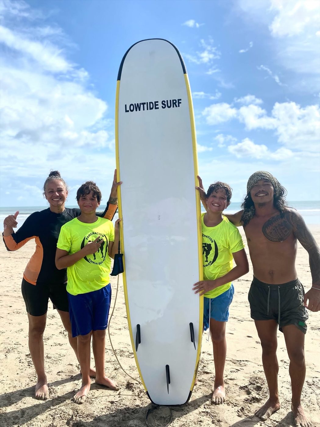 Gov with a family of students and their surfboard on the beach
