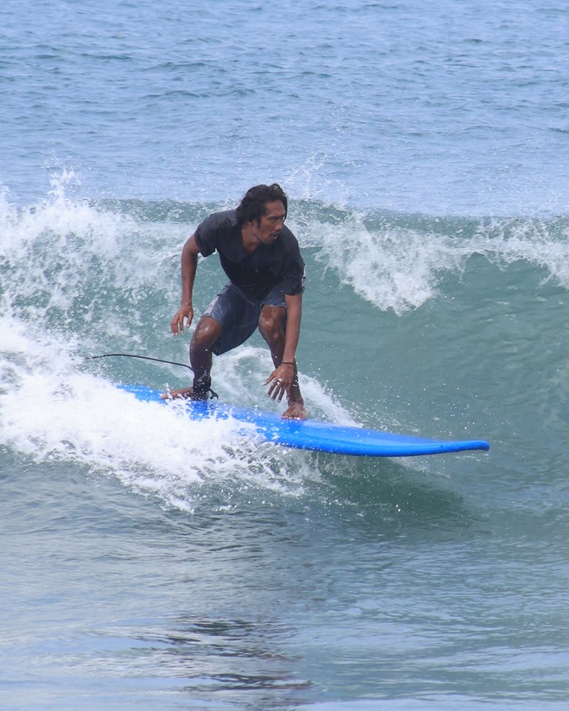 Mika riding a wave on a blue longboard