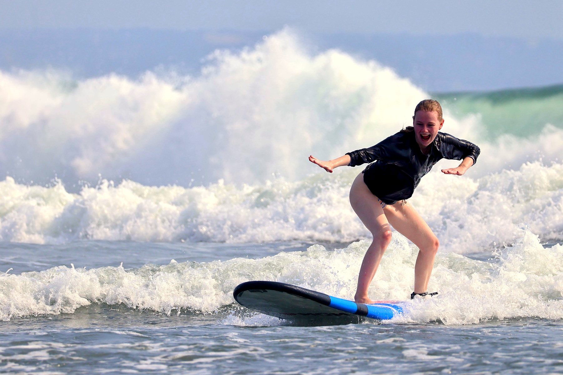 Student riding a wave and laughing on her first stand-up